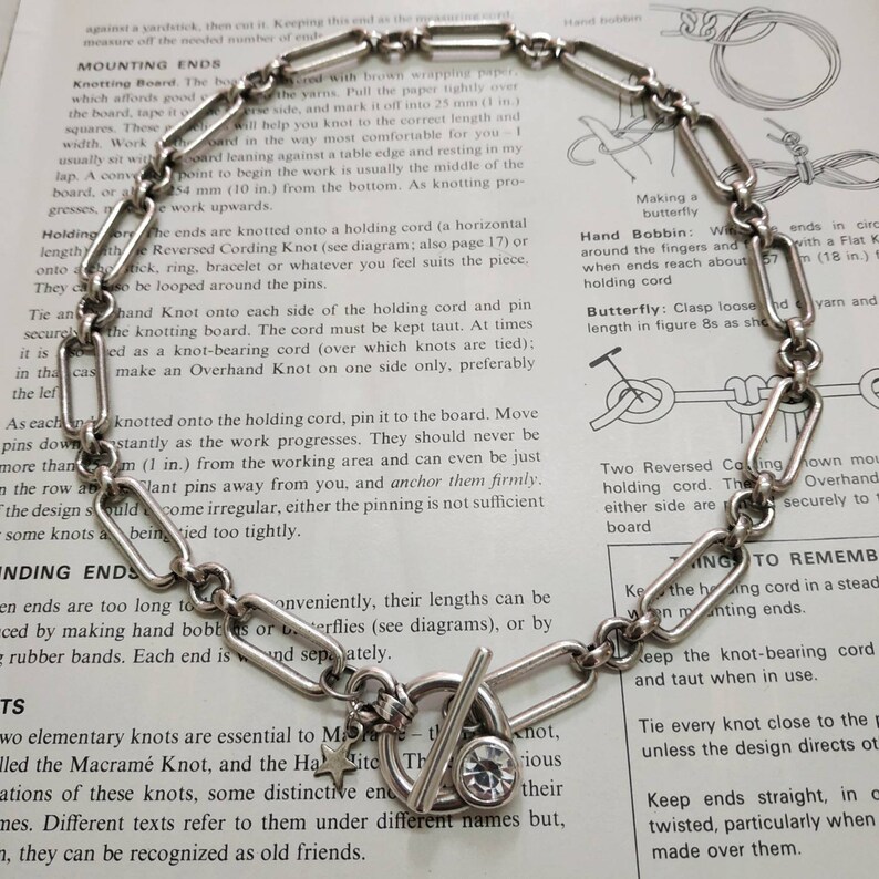 May include: A silver chain necklace with a star charm, a toggle clasp, and a clear rhinestone. The necklace is on a white background with text about knotting techniques.