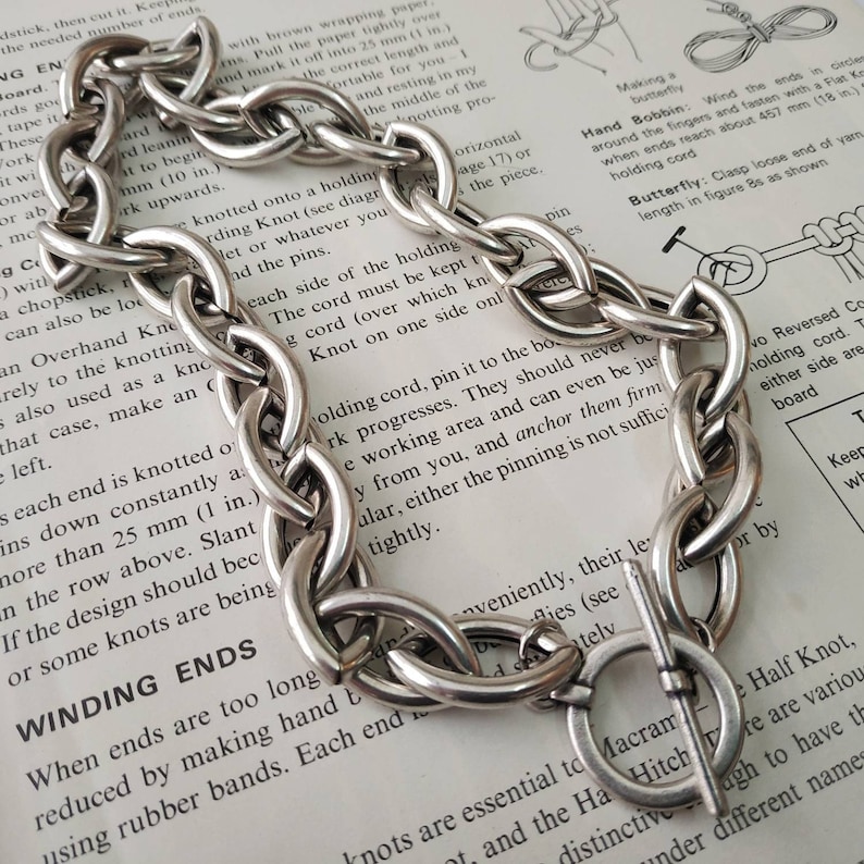 Puede incluir: Un brazalete de cadena de plata con un dise&ntilde;o de eslabones grandes y gruesos. El brazalete tiene un cierre de palanca de plata.