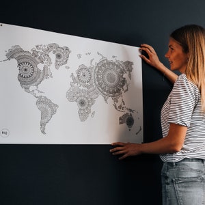 Może przedstawiać: Czarno-biała mapa świata z misternymi wzorami mandali w każdym kraju. Mapa wisi na ciemnoniebieskiej ścianie. Osoba stoi po prawej stronie mapy, trzymając dolny r&oacute;g.