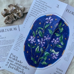 Può includere: Primo piano di una carta stampata con un'illustrazione floreale blu e viola. La carta ha testo in portoghese ed è circondata da altre carte e da un oggetto simile a un osso. L'illustrazione presenta fiori viola e foglie verdi su uno sfondo blu scuro.