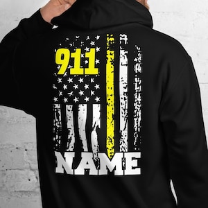 May include: Black hooded sweatshirt with a distressed American flag design featuring a yellow stripe and the text "911" and "NAME".