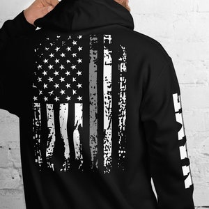 Könnte beinhalten: Schwarzer Kapuzenpullover mit einem abgenutzten amerikanischen Flaggenmuster auf der Rückseite und dem Wort "Brave" auf dem linken Ärmel.