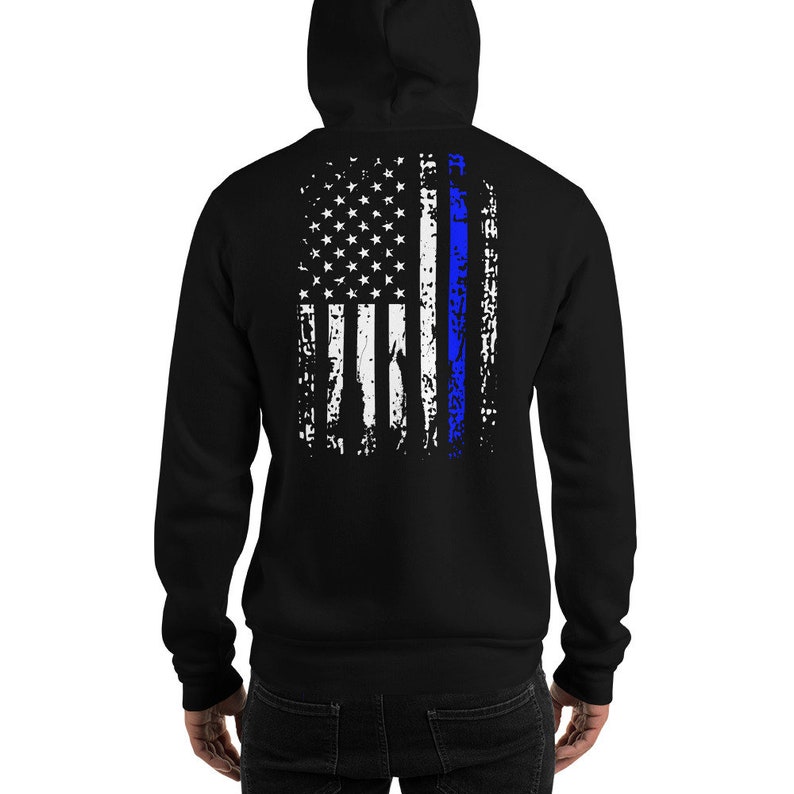 Puede incluir: Sudadera con capucha negra con un dise&ntilde;o de bandera estadounidense desgastado con una l&iacute;nea azul delgada en el centro.