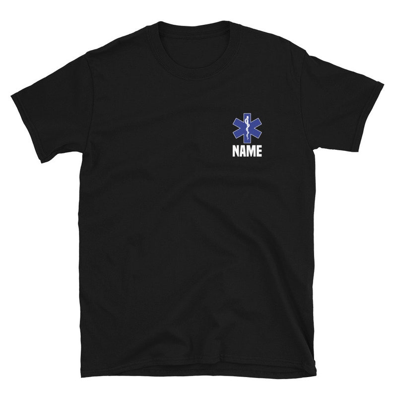 May include: Black t-shirt featuring a blue and white Star of Life emblem, a symbol of emergency medical services. The word "NAME" is printed in white below the emblem. The shirt is made of a soft material.