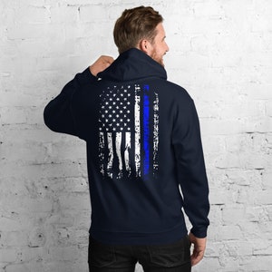 Puede incluir: Una sudadera con capucha azul marino con un dise&ntilde;o de bandera estadounidense desgastado en la espalda. La bandera tiene una fina l&iacute;nea azul que recorre el centro.