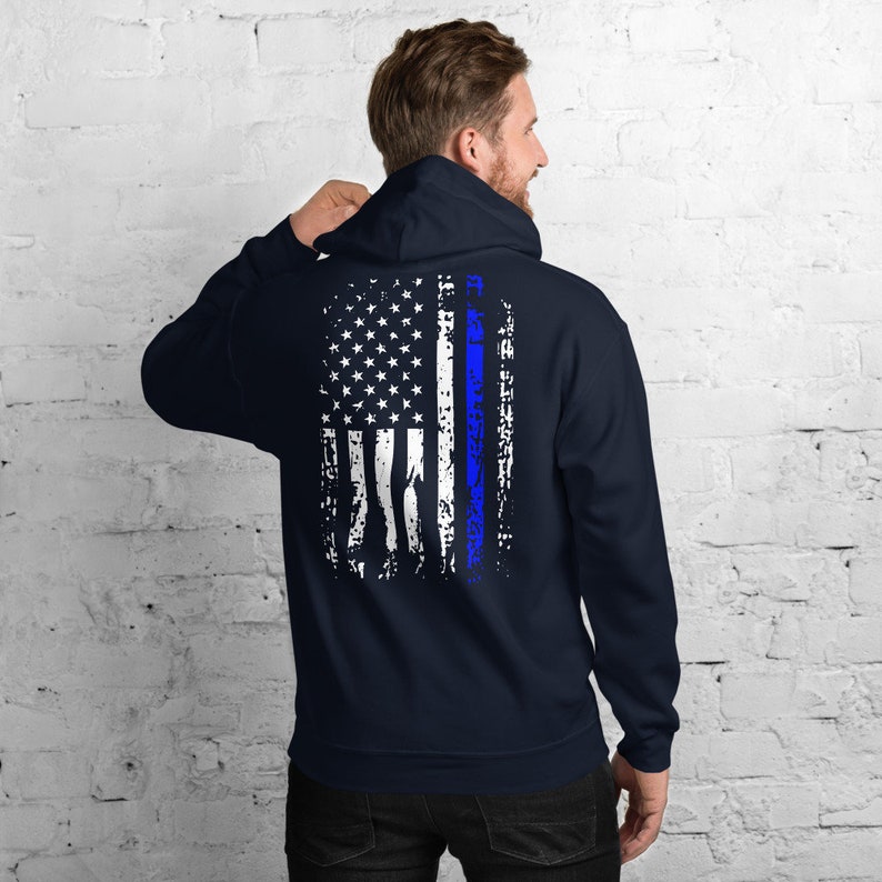 Puede incluir: Una sudadera con capucha azul marino con un dise&ntilde;o de bandera estadounidense desgastado en la espalda. La bandera tiene una fina l&iacute;nea azul que recorre el centro.