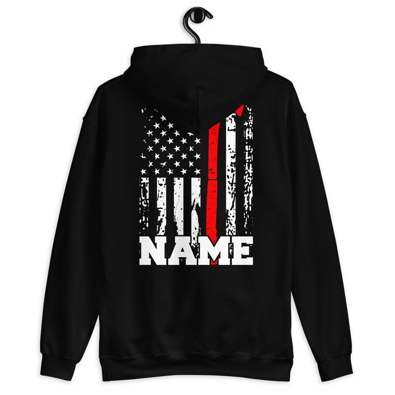 May include: Black hooded sweatshirt with a distressed American flag design featuring a red stripe down the center. The text "NAME" is printed in white below the flag.