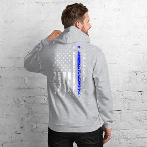 Puede incluir: Una sudadera con capucha gris con un dise&ntilde;o de bandera estadounidense desgastado y una fina l&iacute;nea azul en el centro. La bandera es blanca con estrellas azules.