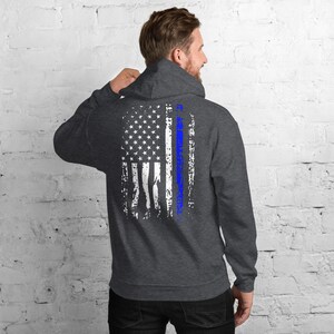Puede incluir: Una sudadera con capucha gris oscuro con un dise&ntilde;o de bandera estadounidense desgastado en la espalda. La bandera es blanca y azul con una fina l&iacute;nea azul en el centro.