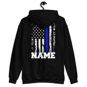 Puede incluir: Sudadera con capucha negra con un dise&ntilde;o de bandera estadounidense desgastado con una l&iacute;nea azul en el centro. El texto "NAME" est&aacute; impreso debajo de la bandera.