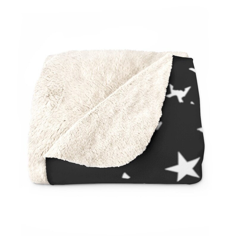 May include: A black and white plush throw blanket with a white star pattern. The blanket is folded in half and the white side is facing the camera.