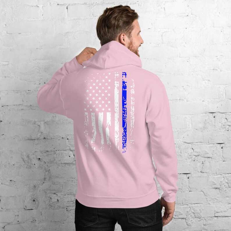 Puede incluir: Una sudadera con capucha rosa con un dise&ntilde;o de bandera estadounidense blanca desgastada y una l&iacute;nea azul en el centro. La sudadera tiene una capucha con cord&oacute;n.