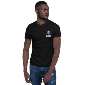 May include: Black t-shirt with a blue and white Star of Life emblem and the word "NAME" printed below it. The shirt is short-sleeved and made of a soft material.