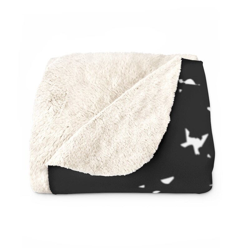 May include: A black and white fleece throw blanket with a pattern of white paper airplanes on a black background. The blanket is folded in half, showing the white fleece lining.
