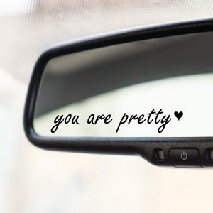 Puede incluir: Un espejo retrovisor con el texto "you are pretty" y un pequeño símbolo de corazón escrito en él.