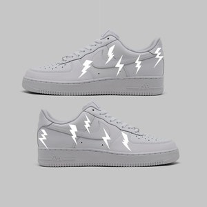 Puede incluir: Zapatillas bajas de cuero blanco con un swoosh Nike blanco y diseños de rayos reflectantes.