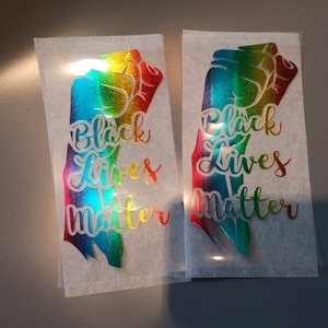 Pode incluir: Dois adesivos de vinil coloridos do arco-íris com um design de punho levantado e o texto "Black Lives Matter".
