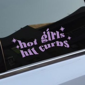Op de afbeelding: Een autoruit met een roze vinyl sticker waarop staat "*hot girls* hit curbs*"