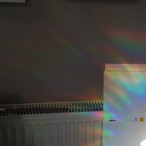 Puede incluir: Un radiador blanco con un prisma de arco&iacute;ris reflej&aacute;ndose en &eacute;l. El prisma est&aacute; unido a una superficie blanca con el texto "Filer" y "2" visible.