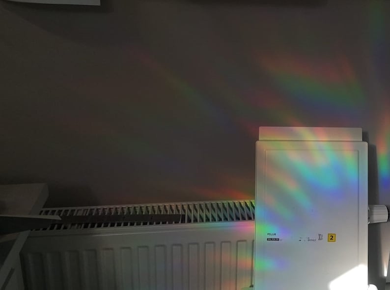 Puede incluir: Un radiador blanco con un prisma de arco&iacute;ris reflej&aacute;ndose en &eacute;l. El prisma est&aacute; unido a una superficie blanca con el texto "Filer" y "2" visible.