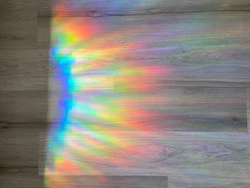 Puede incluir: Un efecto de prisma arco&iacute;ris en un suelo de madera. La luz crea un patr&oacute;n colorido de rojo, naranja, amarillo, verde, azul, a&ntilde;il y violeta.