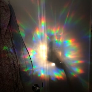 Puede incluir: Una puerta blanca con una luz de prisma arco&iacute;ris reflejada en la superficie. La luz crea un patr&oacute;n colorido de luz y sombra.