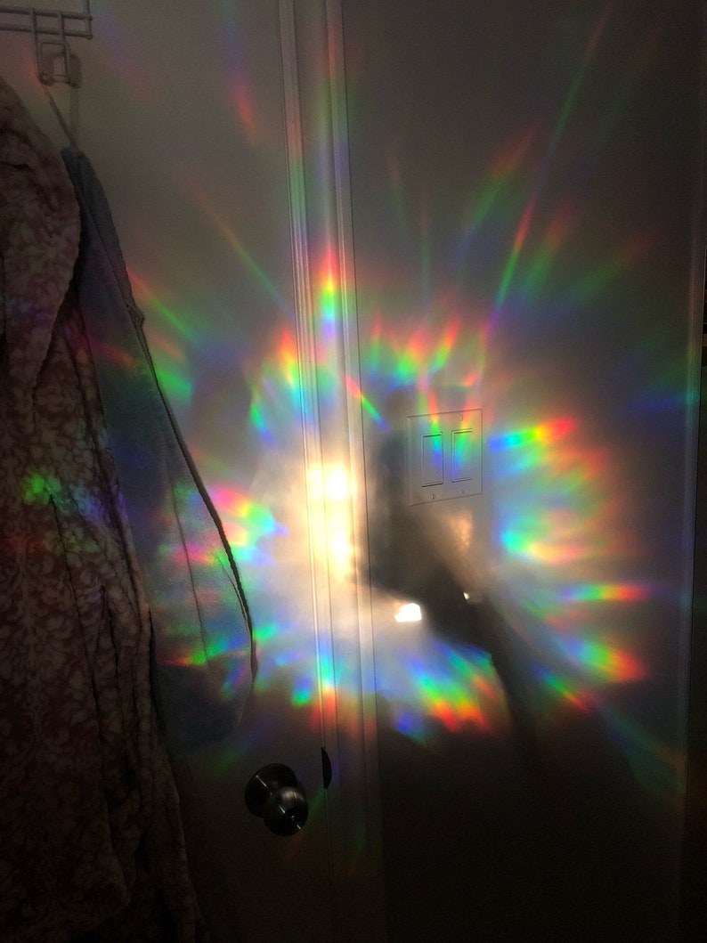Puede incluir: Una puerta blanca con una luz de prisma arco&iacute;ris reflejada en la superficie. La luz crea un patr&oacute;n colorido de luz y sombra.