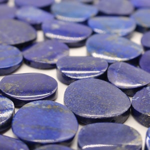 Può includere: Primo piano di numerose pietre di lapislazzuli lucidate, di forma ovale. Le pietre sono di un blu intenso con macchie dorate e bianche. Le pietre sono lisce e hanno una finitura lucida.