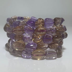 Könnte beinhalten: Ein Armband aus braunen und violetten Edelsteinperlen. Die Perlen sind oval geformt und haben eine glatte, polierte Oberfläche.