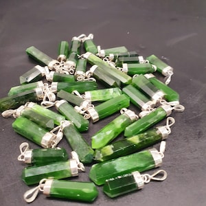 Könnte beinhalten: Ein Haufen grüner Jade-Anhänger mit silbernen Ösen. Die Anhänger sind alle rechteckig und haben eine glatte, polierte Oberfläche.