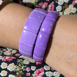 Op de afbeelding: Twee paarse plastic armbanden met een vierkant ontwerp. De armbanden zijn op elkaar gestapeld.