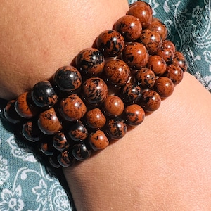 Pode incluir: Um conjunto de pulseiras de pedras preciosas marrons e pretas com um padrão salpicado.