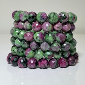 Könnte beinhalten: Ein Stapel grüner und rosafarbener Edelsteinperlen, jede Perle ist facettiert und hat ein einzigartiges Muster. Die Perlen sind auf einer dünnen Schnur aufgereiht.