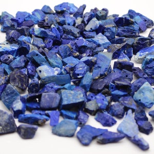 Op de afbeelding: Een verzameling ruwe, diepblauwe lapis lazuli edelstenen. De stenen zijn van verschillende grootte en vorm, sommige met gouden insluitsels. Veel hebben kleine gaatjes, mogelijk voor sieraden of knutselprojecten. Afmetingen in cm.