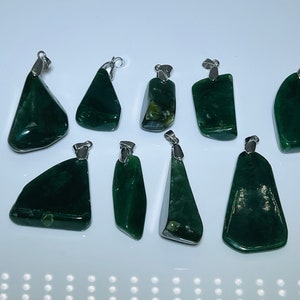 Può includere: Un set di nove ciondoli in giada verde con anelli di balla in argento. I ciondoli sono tutti di forme e dimensioni diverse e hanno una finitura naturale e lucida.