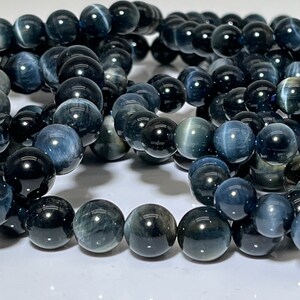 Può includere: Una collana di perle di pietra preziosa blu scuro e grigia. Le perle sono rotonde e hanno una finitura liscia e lucida.