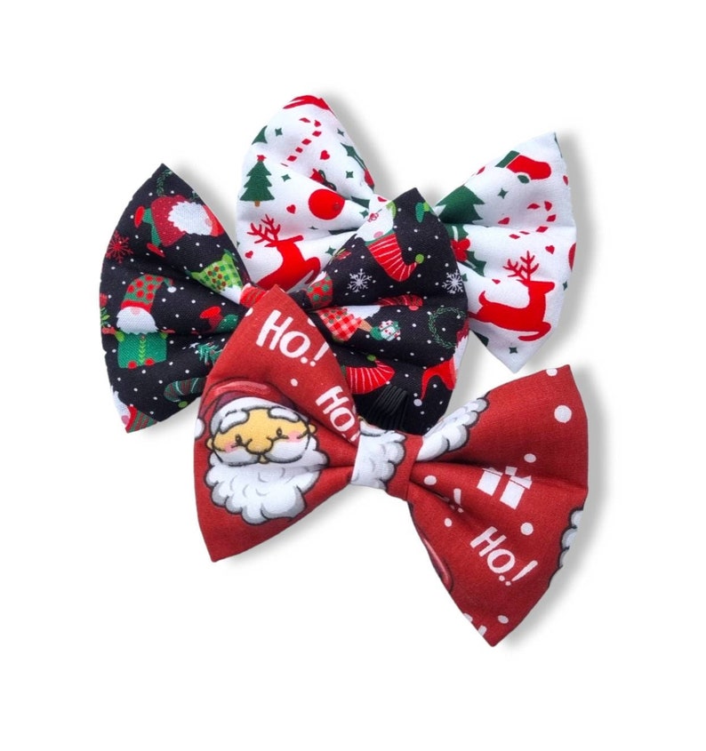 May include: Three Christmas-themed fabric bow ties. One is red with white snowflakes and the text "Ho! Ho!" Another is black with green and white Christmas characters and the text "Ho! Ho!" The third is white with red reindeer and red hearts.