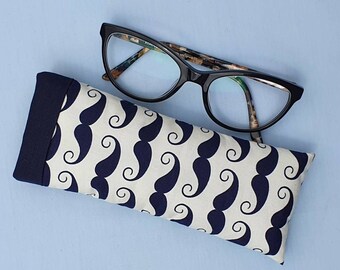 May include: A white and navy blue patterned glasses case with a black trim. The case has a repeating pattern of navy blue moustaches.