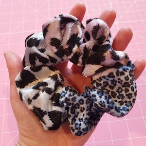 Op de afbeelding: Een set van drie scrunchies in verschillende dierenprintpatronen. De scrunchies zijn gemaakt van een zachte, fluweelachtige stof en zijn in tinten blauw, paars en zwart.