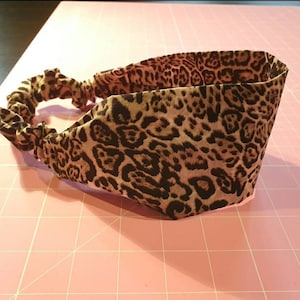 May include: A brown and black leopard print headband with a gathered elastic band.