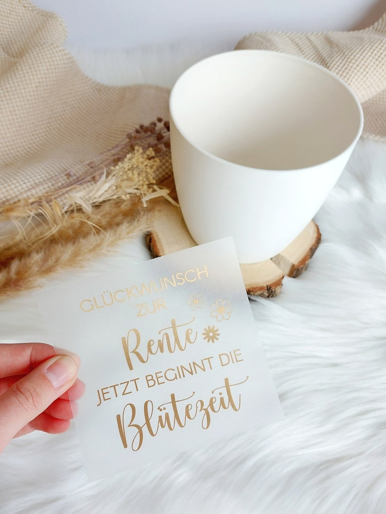 May include: A white card with gold lettering that reads "Gl&uuml;ckwunsch zur Rente* Jetzt beginnt die Bl&uuml;tezeit".