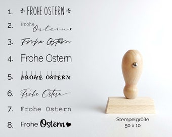 May include: Eight different variations of the phrase "Frohe Ostern" (Happy Easter in German) are shown in black text on a white background. A wooden rubber stamp with a 50 x 10 cm size is also shown.