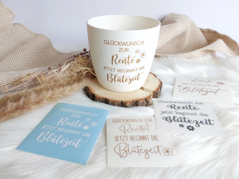 May include: A white ceramic mug with gold lettering that reads "Gl&uuml;ckwunsch zur Rente! Jetzt beginnt die Bl&uuml;tezeit" which translates to "Congratulations on your retirement! Now the bloom time begins".