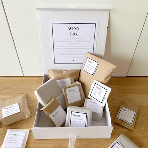 Könnte beinhalten: Eine weiße Box gefüllt mit kleinen braunen Papiertüten, jede mit einem kleinen schwarzen Etikett, auf dem "Wenn..." steht, gefolgt von einem kurzen Satz. Die Box ist geöffnet und die Tüten sind in einem ordentlichen Muster angeordnet. Die Box steht auf einer Holzoberfläche.