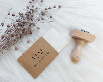 May include: A brown envelope with a white envelope inside. The brown envelope has the text "A|M ANNA & MARCEL" printed on it. A wooden stamp with a black ink pad is also shown.