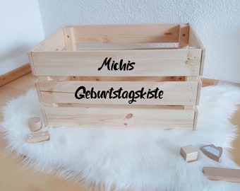 May include: A wooden crate with the words "Michis Geburtstagskiste" written on it. The crate is sitting on a white fluffy rug.