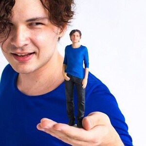 May include: A person holding a small blue figurine of another person in their hand. Both figures are wearing blue shirts.