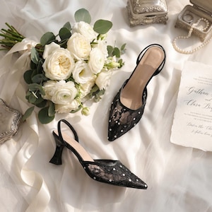 Elegant lace slingback heels with pointed toe and sculpted heel, available in white and black colors, styled in romantic bridal setting with pearls, lace fabric, and floral details for wedding or special occasion wear.