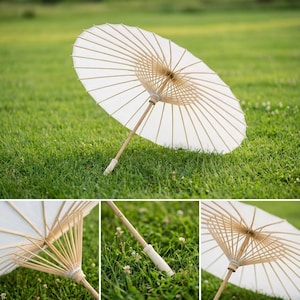 May include: A white paper parasol with a bamboo handle and ribs, resting on green grass. The parasol is open, showcasing its delicate design. The handle has a white grip. The image is well-lit, highlighting the parasol's texture and form.