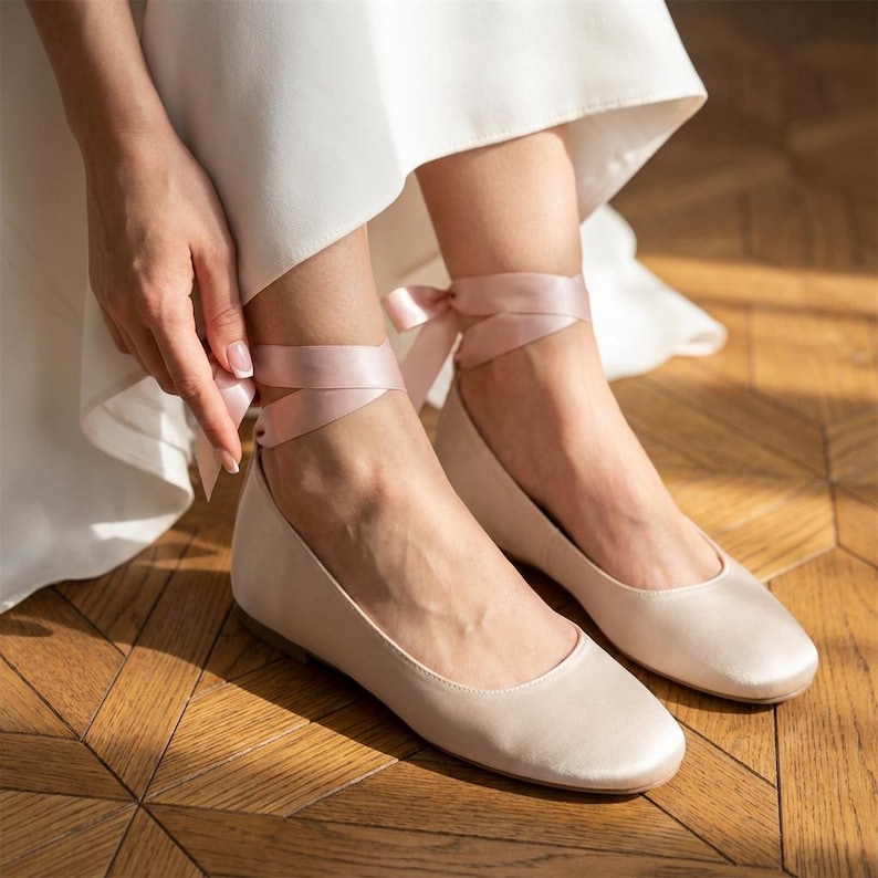 Bridal ballet flats with ribbon ties in soft blush satin, comfortable wedding shoes for bride, minimalist flat shoes for ceremony and reception, elegant lightweight bridal footwear on wooden floor